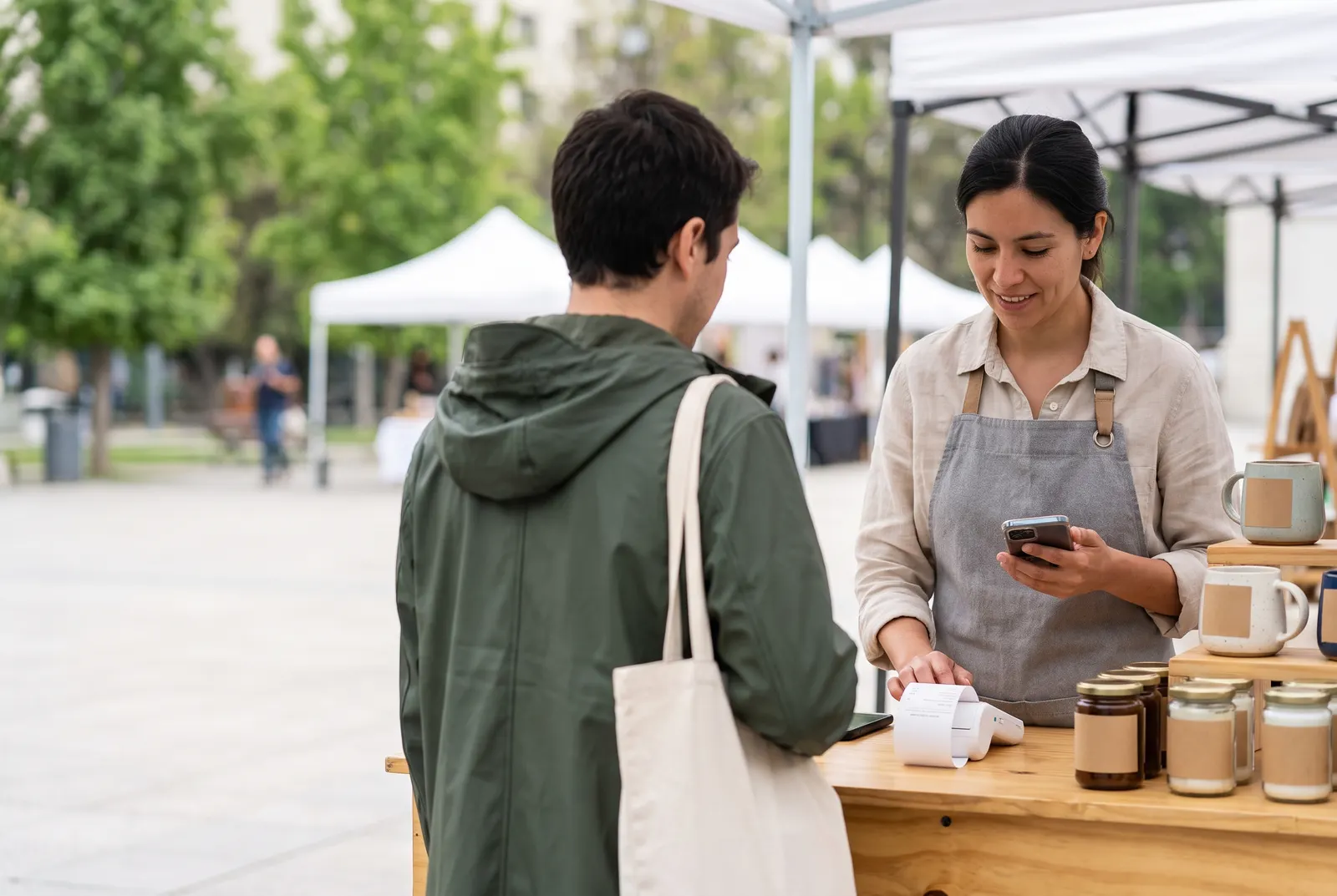 Vendedor en una feria cobra con el celular y una impresora de boletas portátil